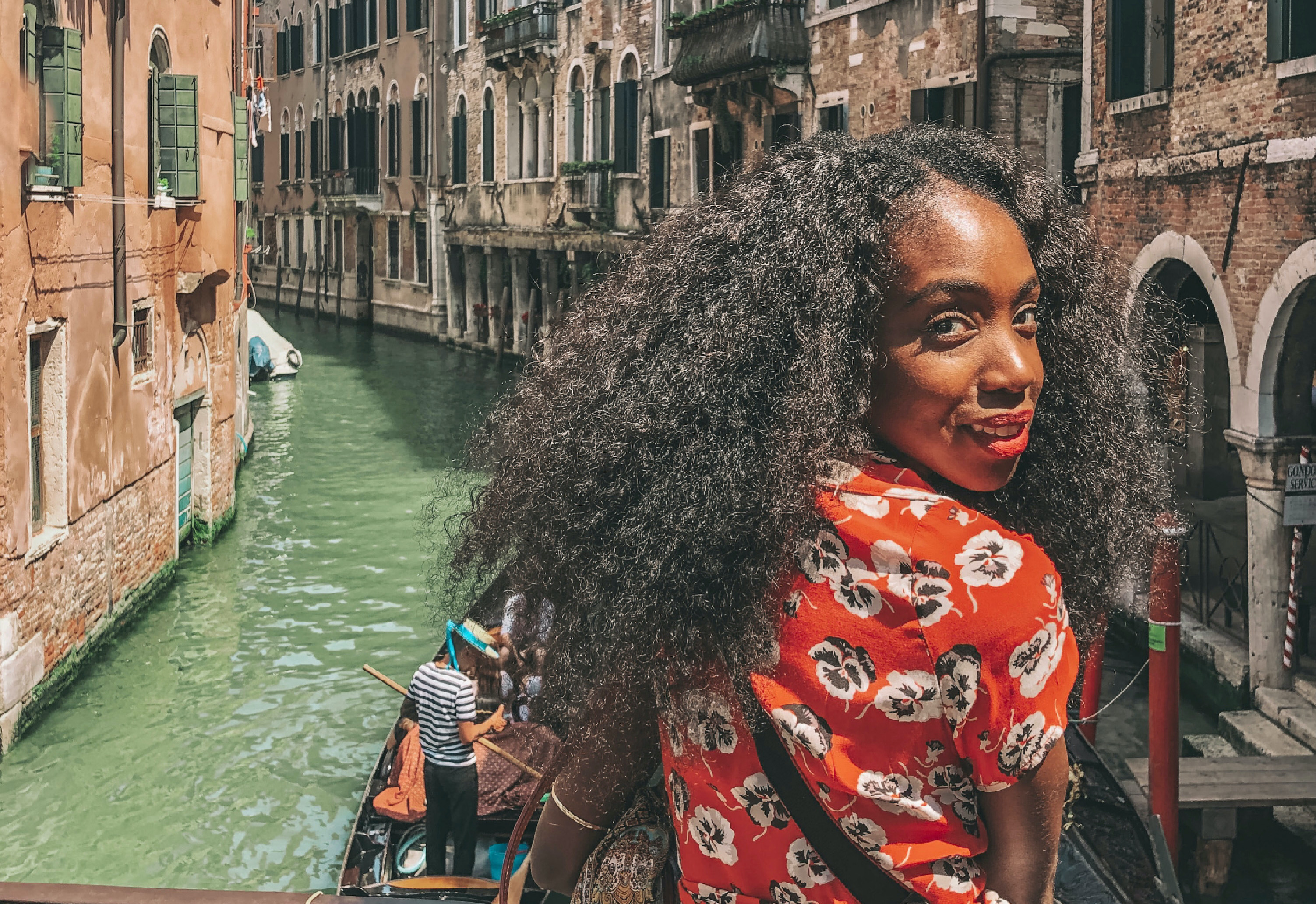 Black woman looking over her shoulder in floral dress in Venice with water and gondolier in background